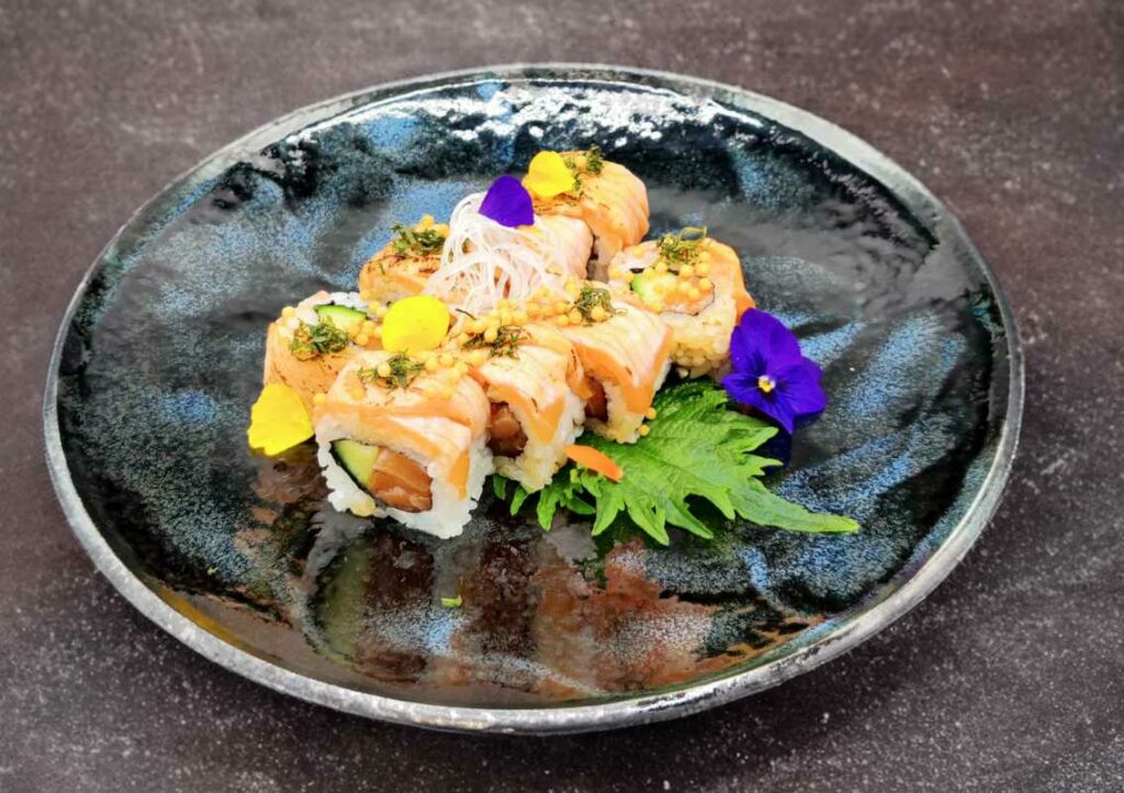 Uramaki Sushi au saumon avocat dans une assiette noire avec feuille de shizo et une fleur violette