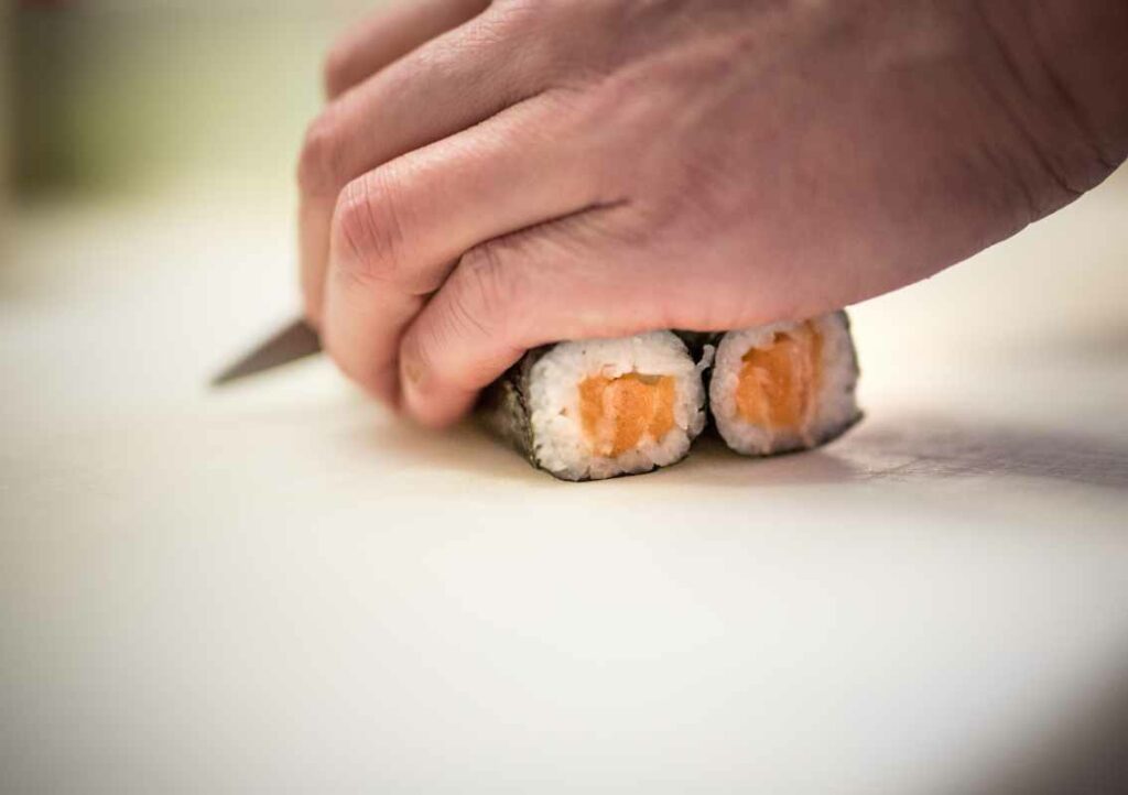 Mains qui découpent Sushi Maki au saumon