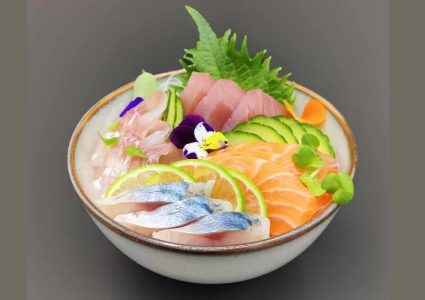 Sashimi dans un bol beige avec des tranches de saumon de dorade de maquereau et de thon des feuilles de shizo du citron des concombres et des fleurs